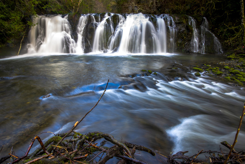 Wide multi-tiered waterfall spreading across a rocky ledge into a still pool below